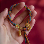 Close up of golden Tibetan prayer wheel charm on colorful woven string bracelet
