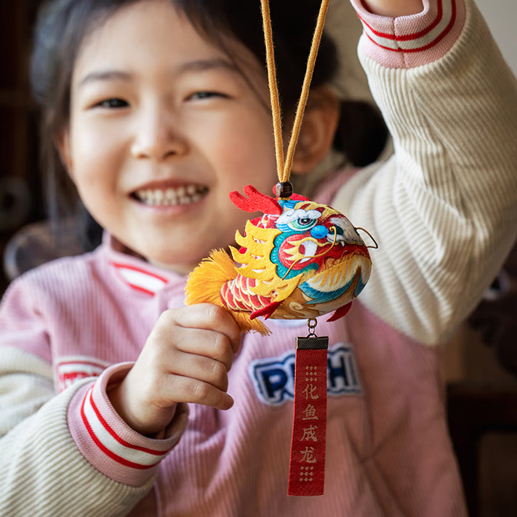 Smiling girl holding a handmade cute silk dragon carp sachet pendant with red blessing tag