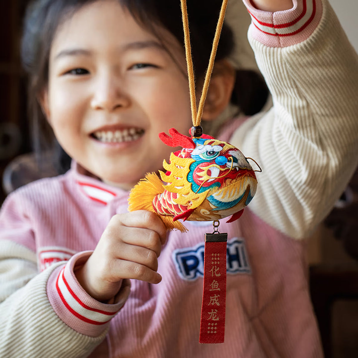 Smiling girl holding a handmade cute silk dragon carp sachet pendant with red blessing tag