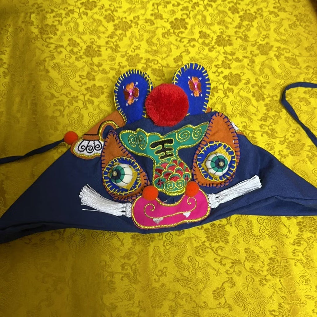 Close up of vibrant hand-embroidered tiger face features and cotton ear flaps on traditional folk hat