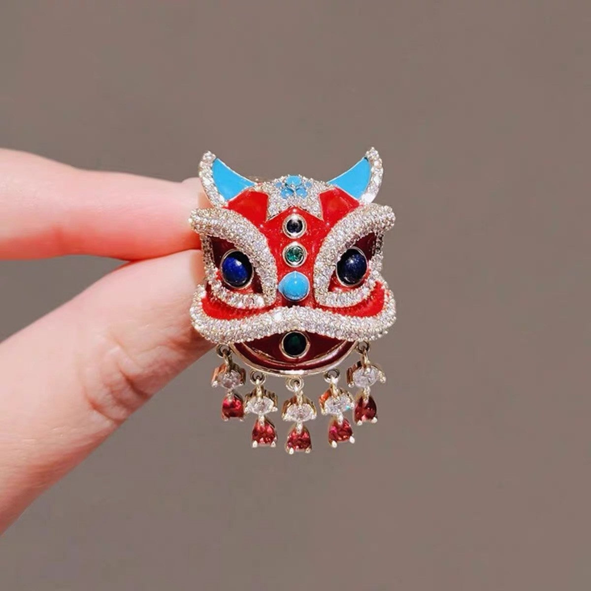 Close up of red enamel and faux rhinestone details on oriental lion dance suit lapel pin