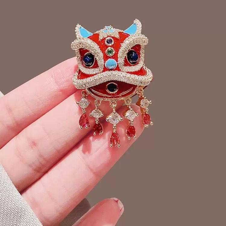 Close up of red enamel and faux rhinestone details on oriental lion dance suit lapel pin